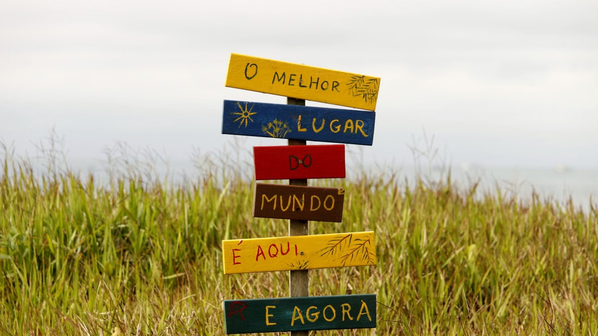 Vibrant multilingual sign in a grassy field in Guaratuba, Paraná, Brazil, showcasing local charm.